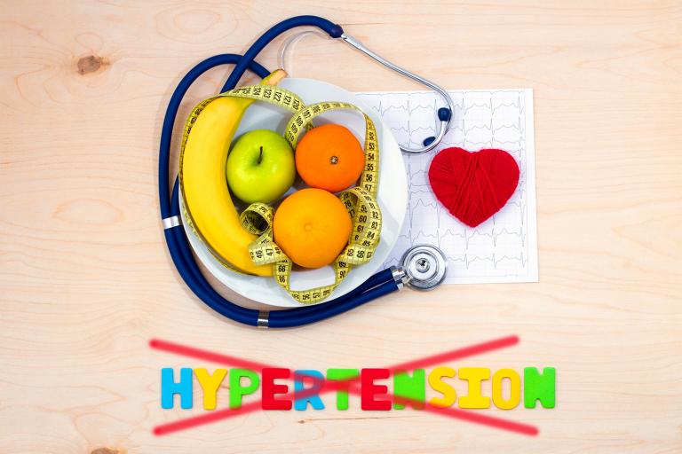 A bowl of fruit, measuring tape, and a stethoscope on a cardiac chart