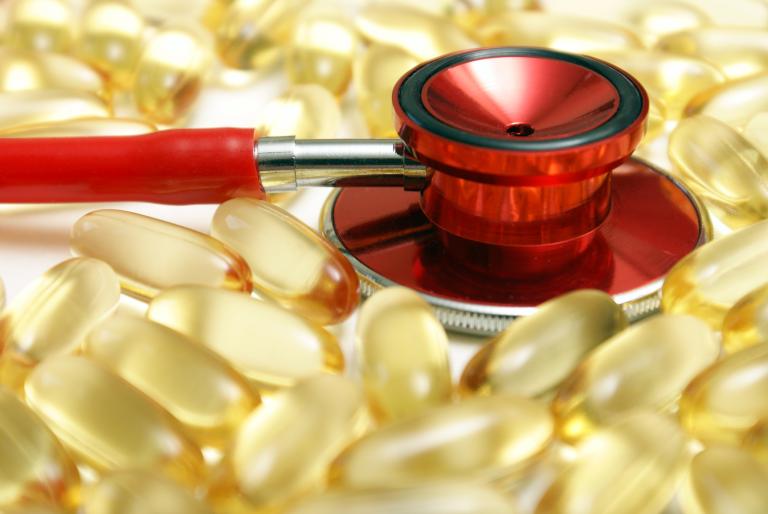 Red stethoscope resting on omega 3 capsules.